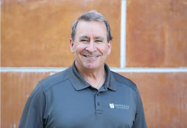 Orthodontist in Brentwood, CA, Dr. Sheffield smiling in his gray Sheffield & Le polo