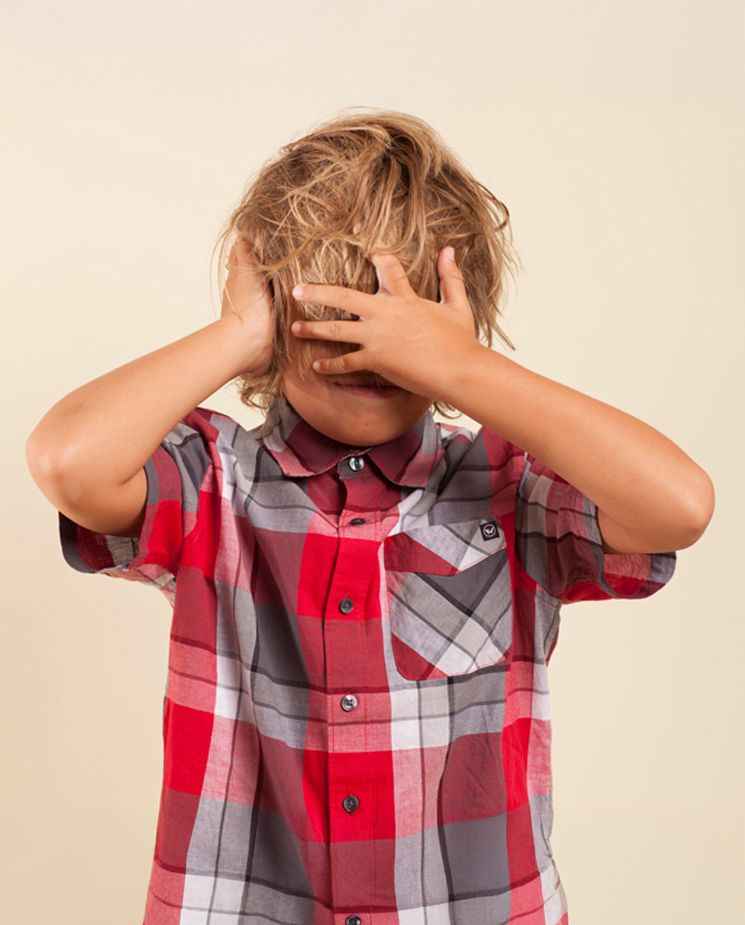 Boy in red and gray plaid covering his eyes with his hair and face