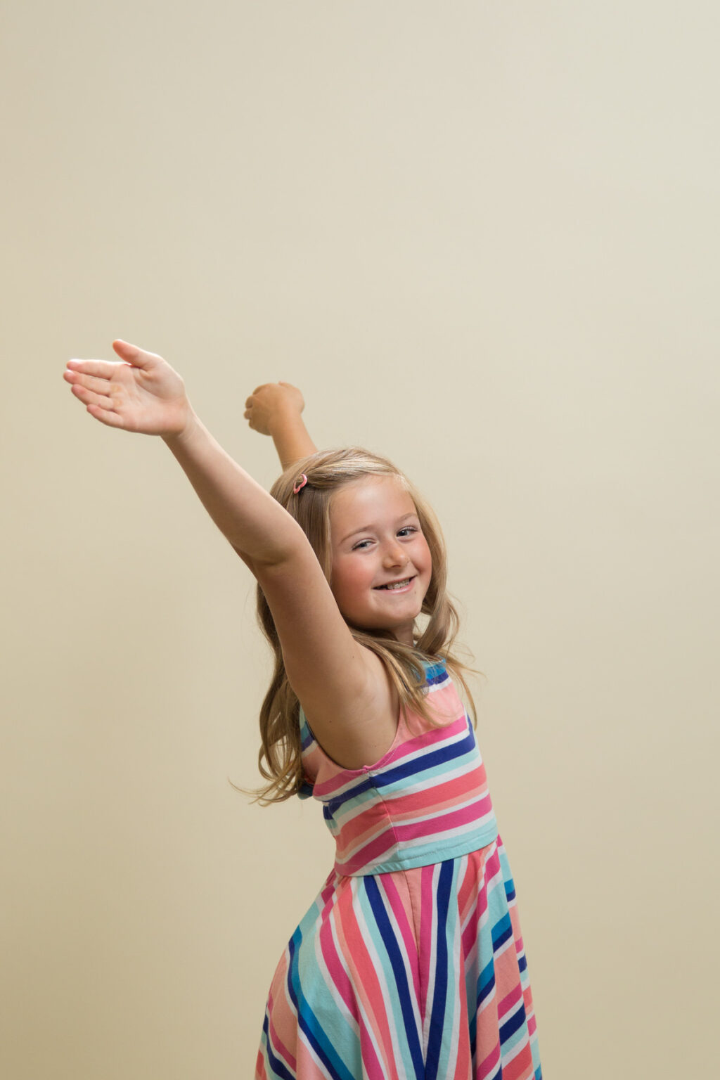 Girl smiles and throws her hands up in the air while her dress flows