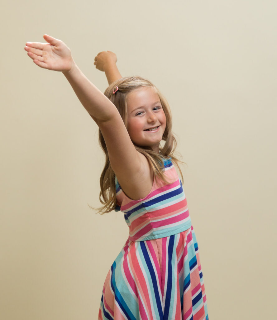 Girl smiles and throws her hands up in the air while her dress flows