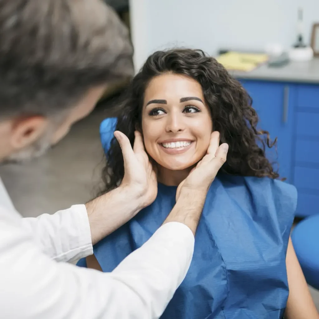 Dentist examining a smiling woman in a dental chair wearing a blue protective bib.