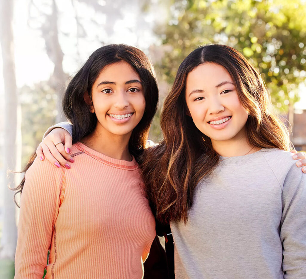 Two teenagers standing outside wearing clear braces.